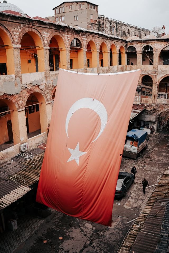 A large Turkish flag hangs in a historic Istanbul courtyard, showcasing classical Ottoman architecture.