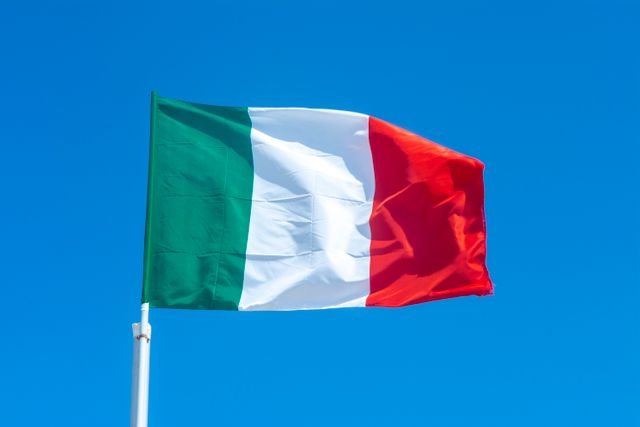 The Italian flag waves vibrantly against a clear blue sky, symbolizing national pride.